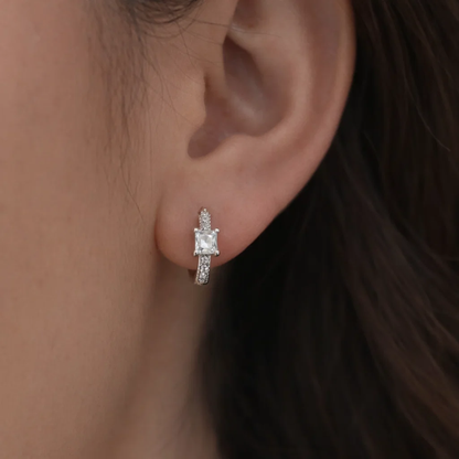 Silver square-cut huggie hoop earrings on ear with clear center stone