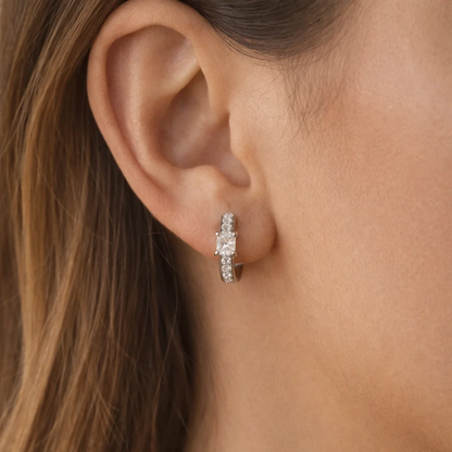 Silver square-cut huggie hoop earrings on ear with clear rectangular stones