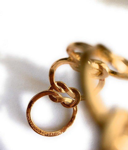 Gold love-knot bracelet close-up with oval charm tag on chain links