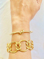 Gold love-knot bracelet on wrist with chain link cuff and knot bangle