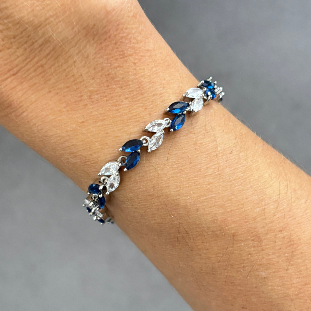 Silver tennis bracelet on wrist with alternating blue marquise and clear cubic zirconia