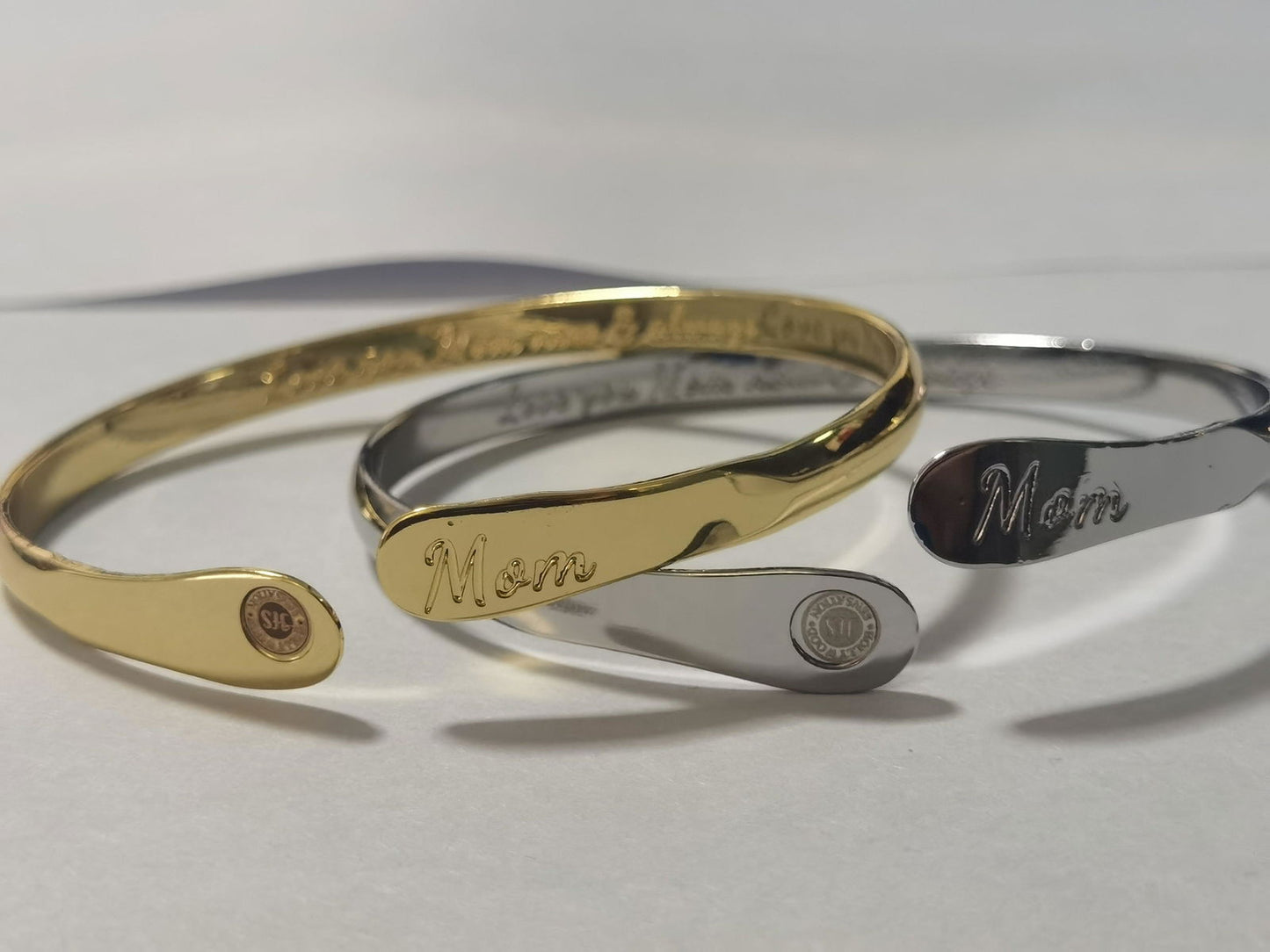 Set of gold and silver mom bangle bracelets with oval “Mom” engravings and round emblems