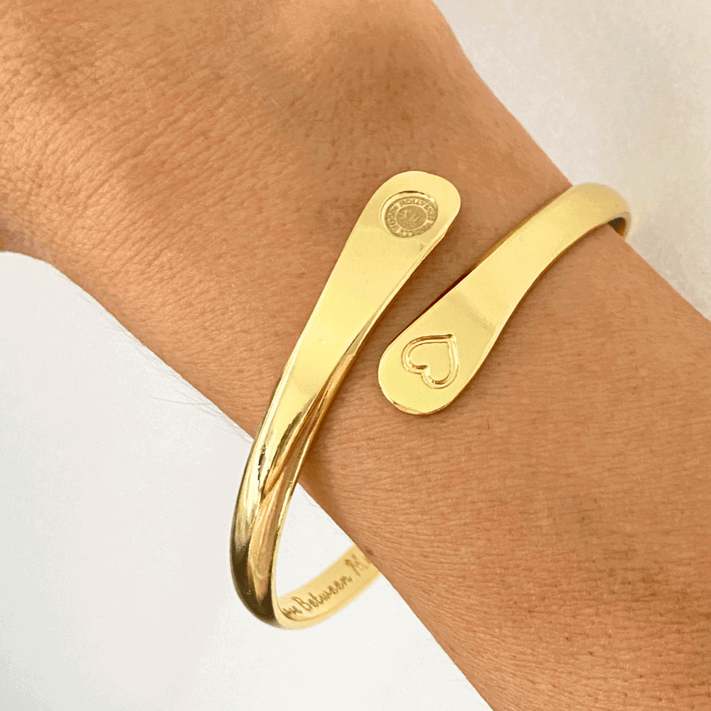 Gold engraved cuff bracelet on wrist with heart and round logo charms