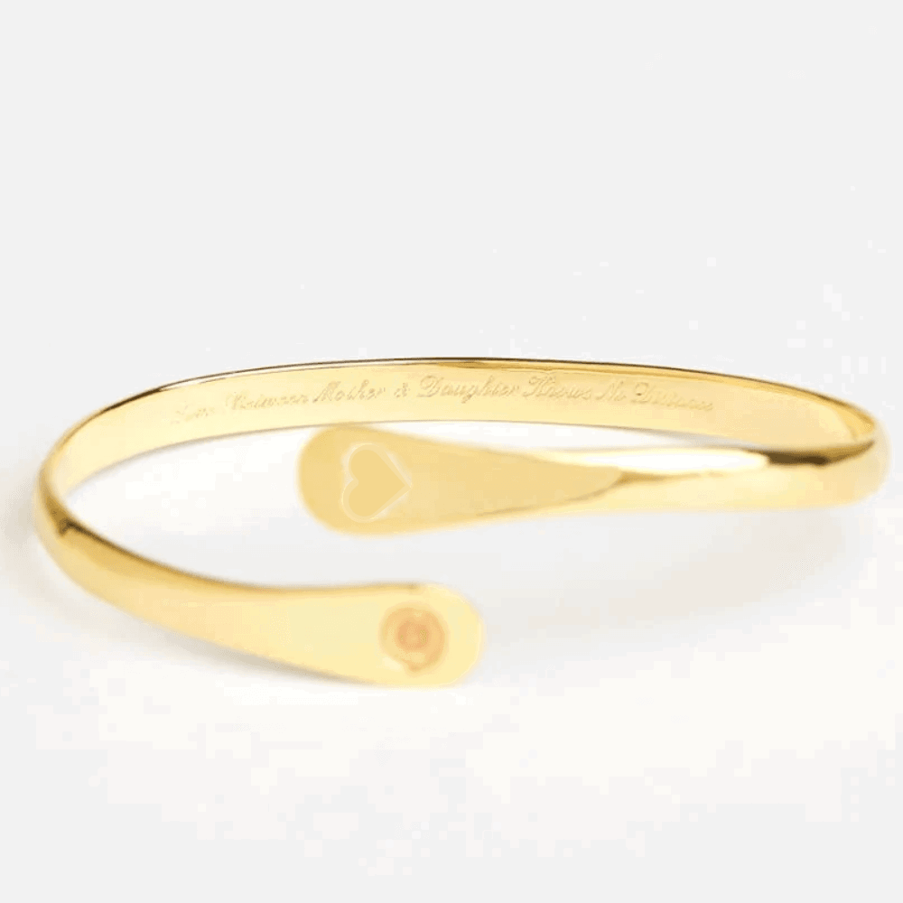 Gold engraved cuff bracelet with heart cutout and round logo medallion