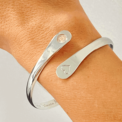 Silver engraved cuff bracelet on wrist with heart and round logo charms