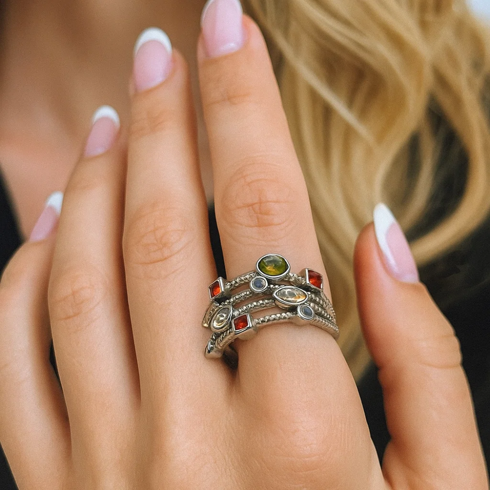 Silver-tone multicolor gemstone ring on hand with green, gold, and clear stones