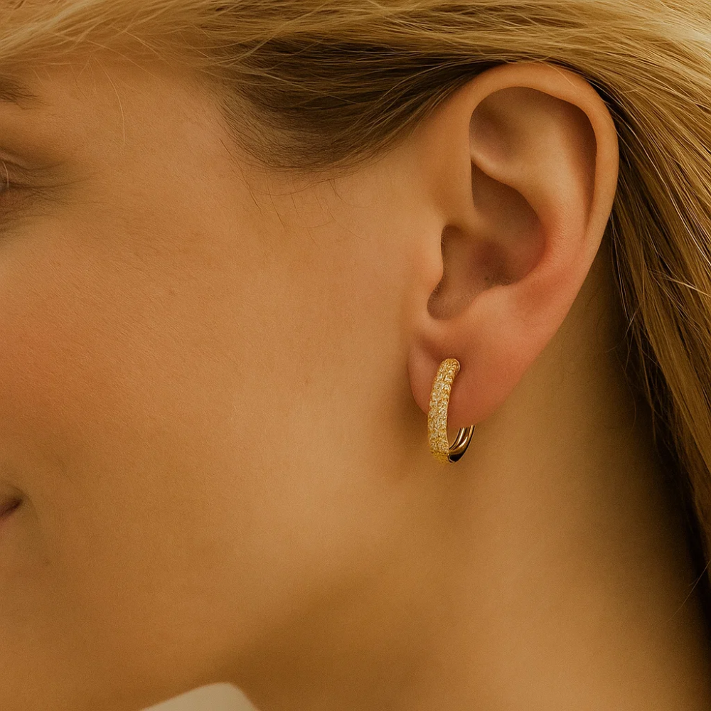 Gold pavé huggie hoop earring worn in the earlobe