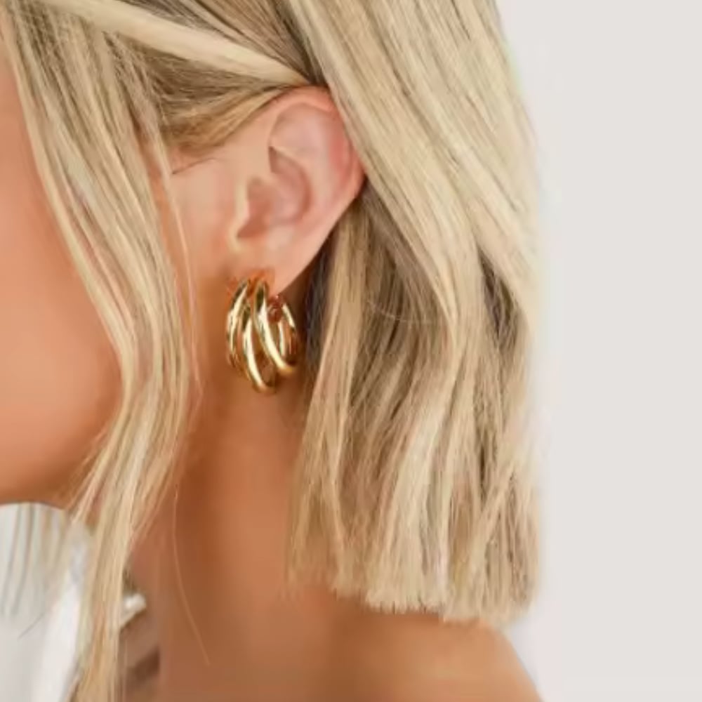 Gold triple huggie hoop earrings on ear, stacked hoops with small charm detail