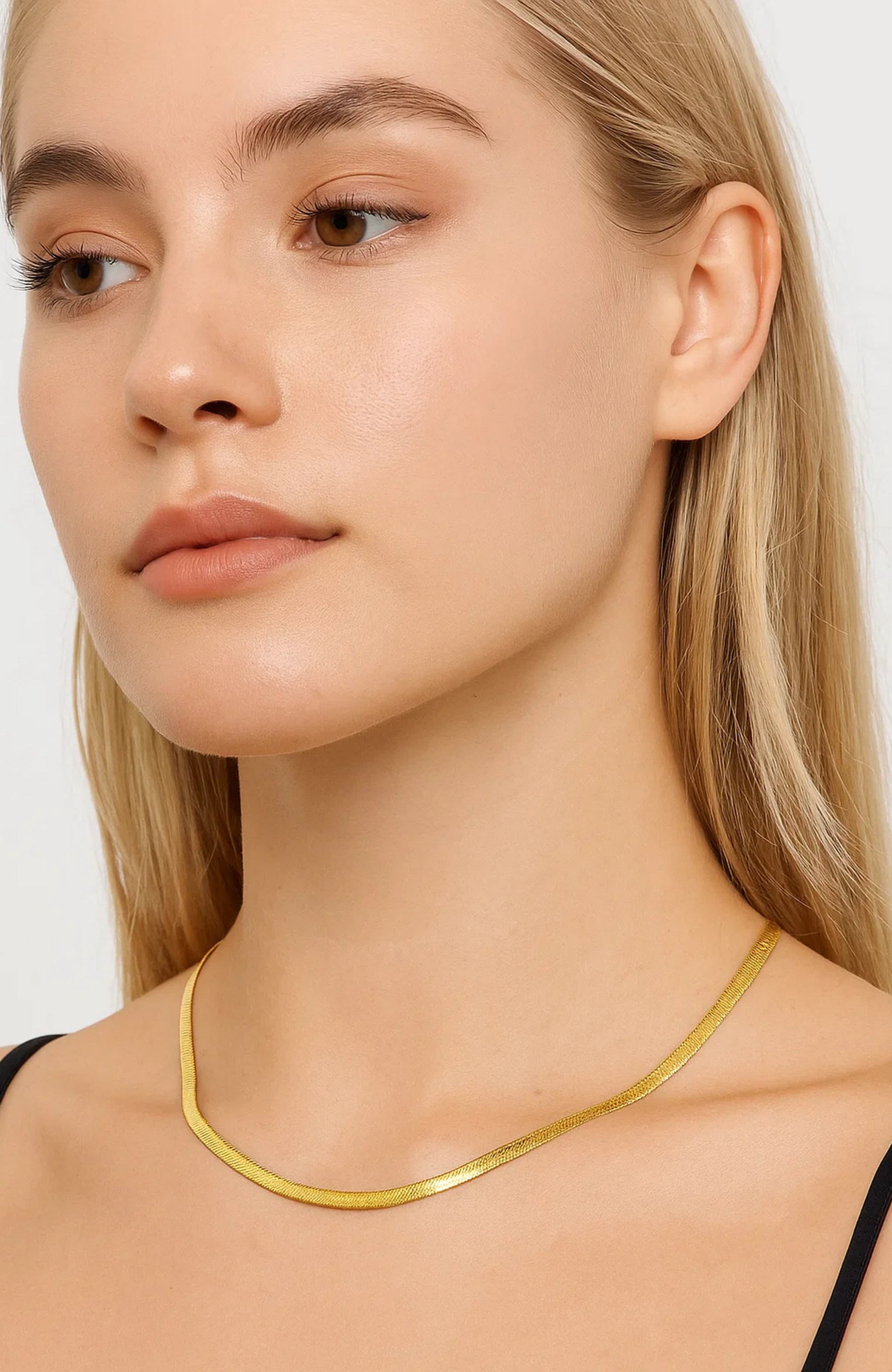 Gold snake chain necklace on collarbone, close-up of slim curved links