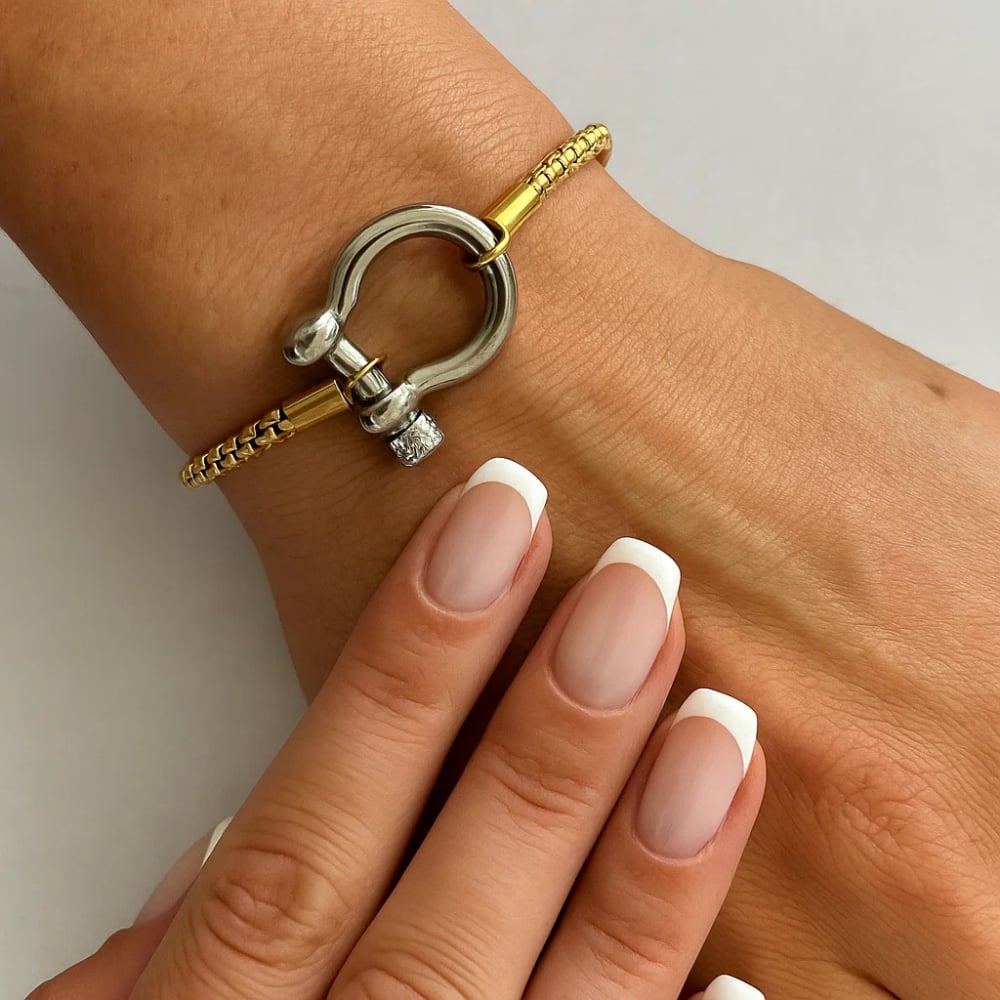 Two-tone bracelet on wrist: silver horseshoe carabiner clasp with gold chain links.