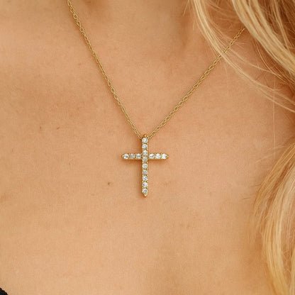 Gold-tone cross pendant necklace with small CZ stone accents, close-up on skin
