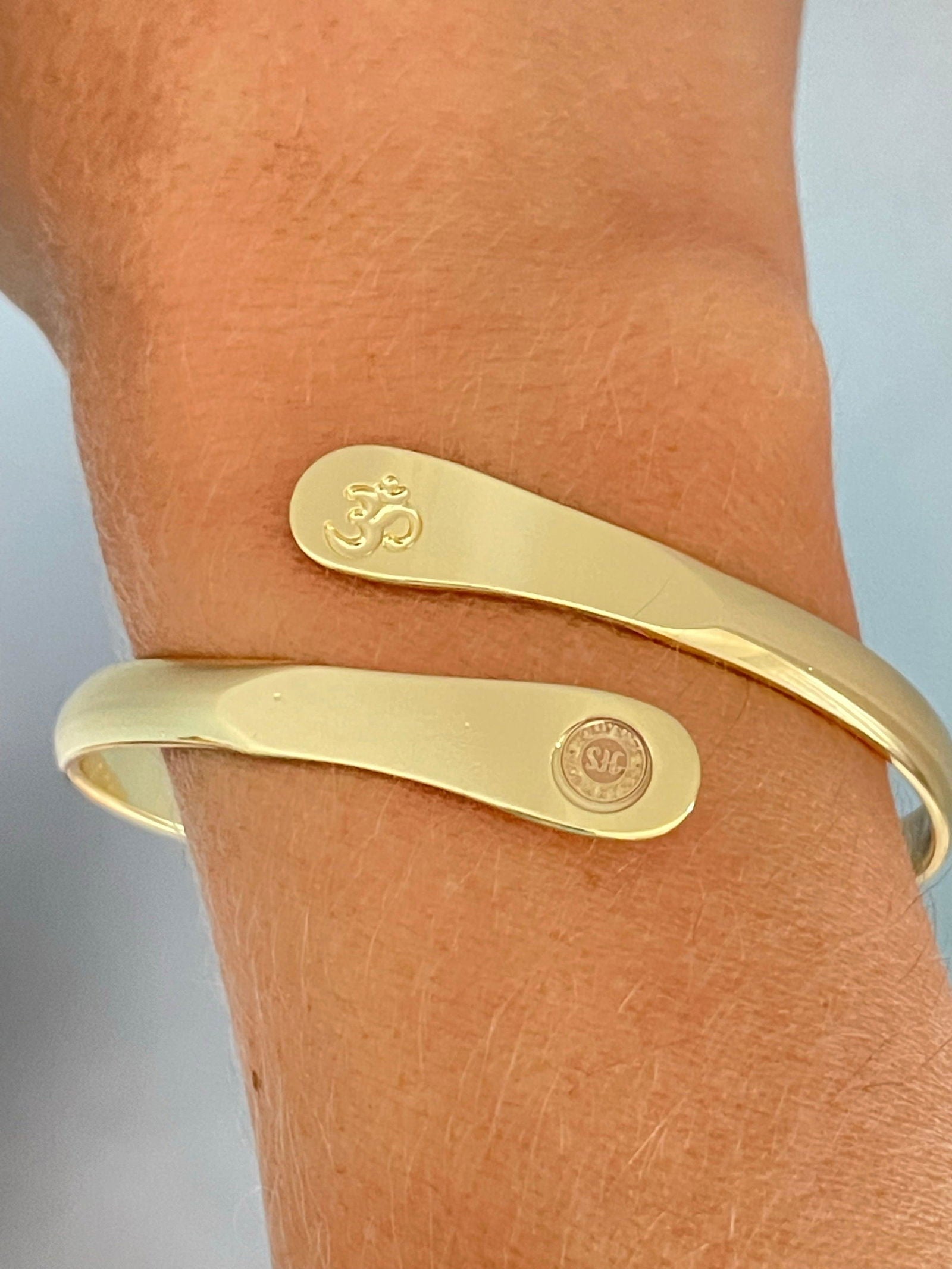 Gold yoga bracelet on wrist with engraved Om symbol and small round logo panel