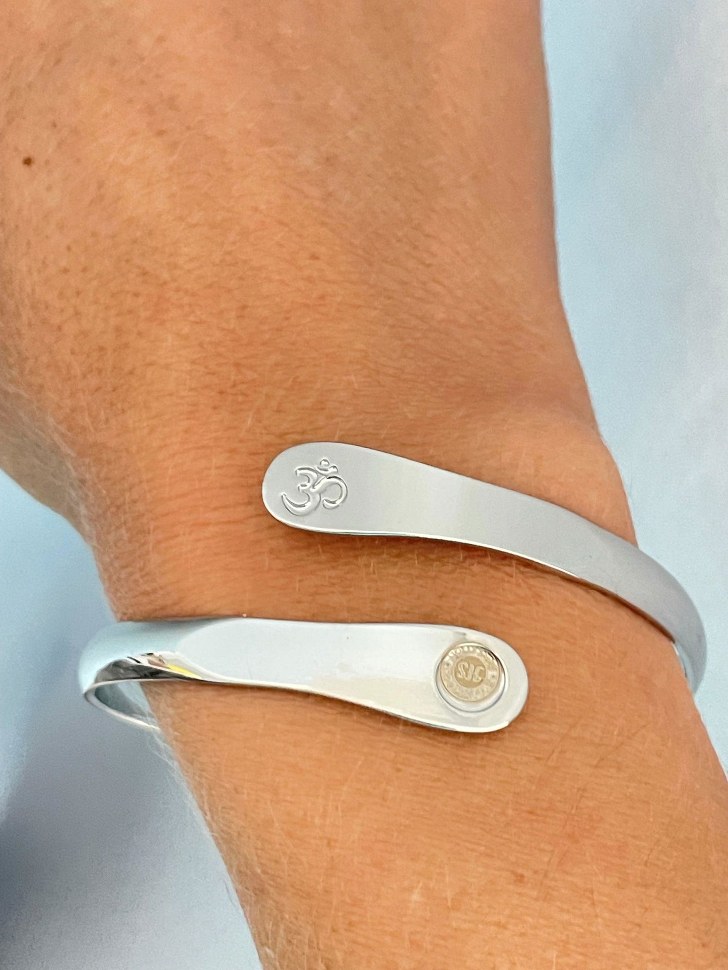 Silver yoga bracelet on wrist with engraved Om symbol and small round logo panel