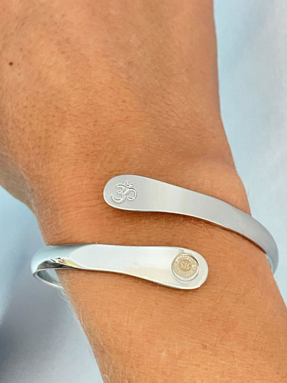 Silver yoga bracelet on wrist with engraved Om symbol and small round logo panel