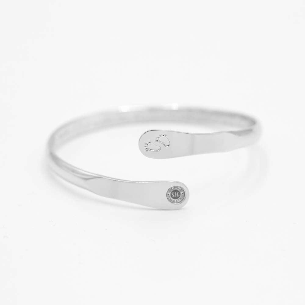 Silver baby footprint engraved bangle bracelet with oval footprint charm and small round logo.