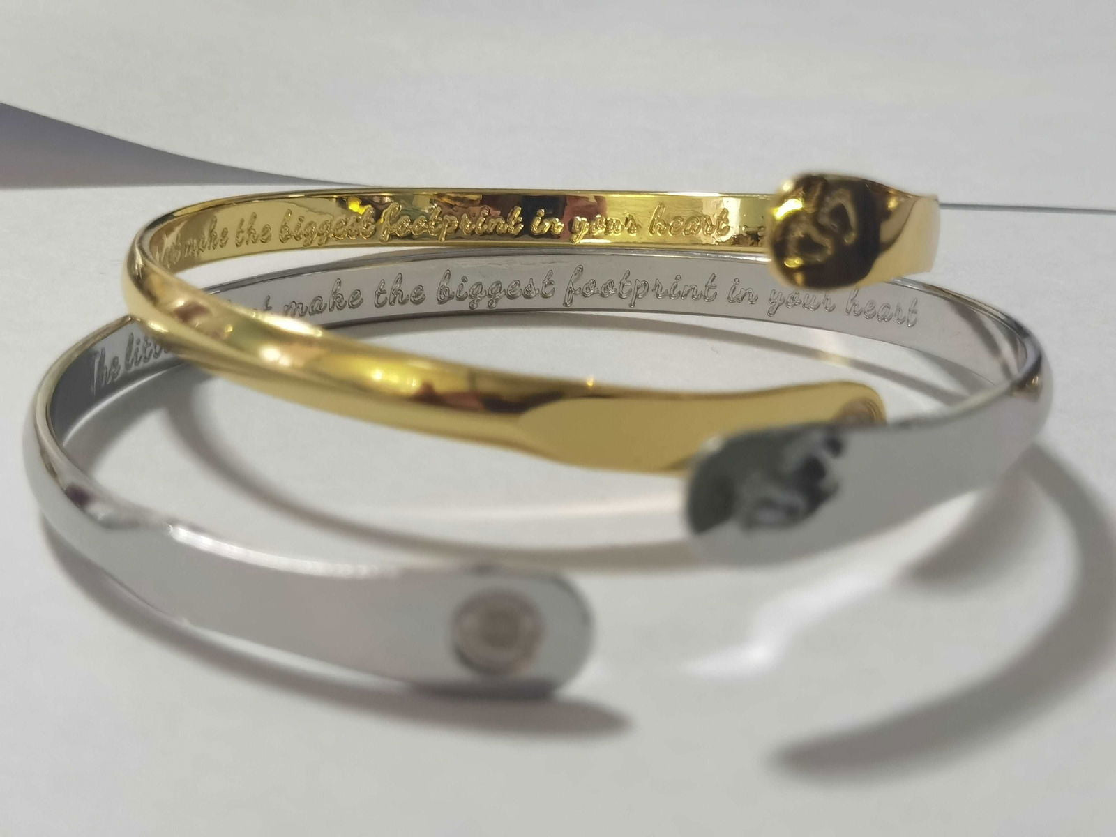 Pair of baby footprint bangle bracelets in silver and gold, each with an oval footprint charm.