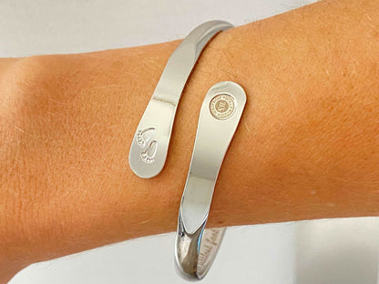 Silver baby footprint bangle bracelet worn on wrist, smooth cuff with stamped motif