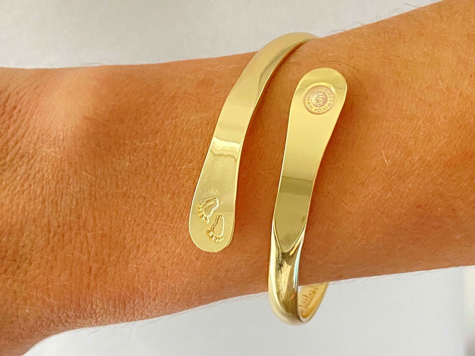 Gold baby footprint bangle bracelet worn on wrist, smooth cuff with stamped motif