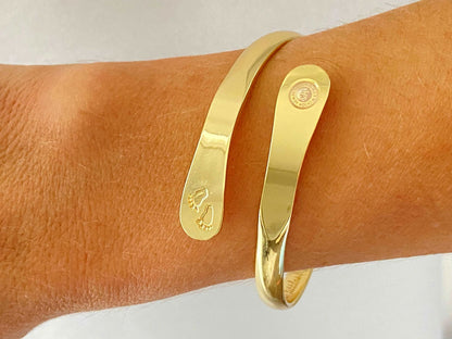 Gold baby footprint bangle bracelet worn on wrist, smooth cuff with stamped motif