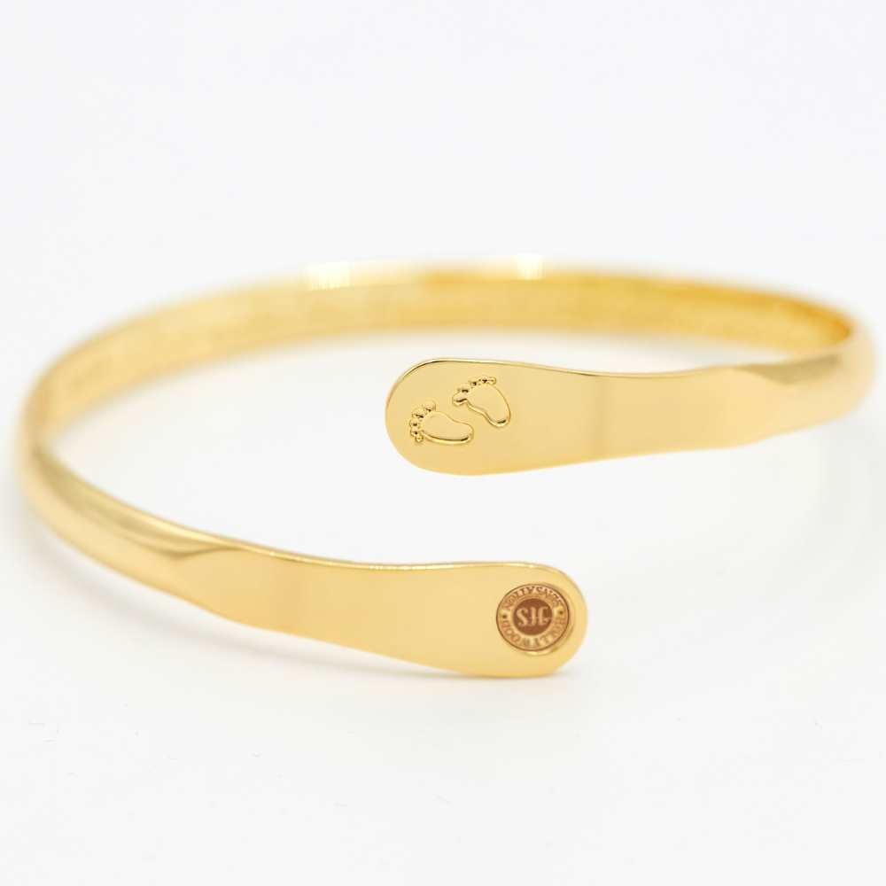 Gold baby footprint engraved bangle bracelet with circular hallmark on cuff end