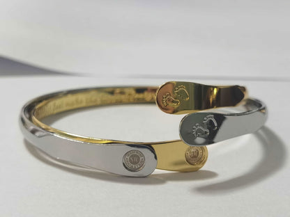 Two-tone baby footprint bangle bracelets: one silver, one gold, each with oval footprint charm.
