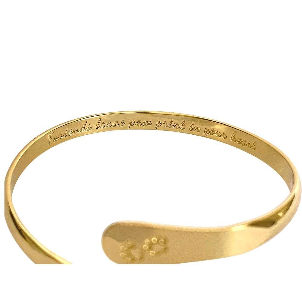 Gold cuff bracelet with paw print engraving on inner plate and logo medallion