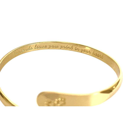 Gold cuff bracelet with engraved message along the band and paw plate inside