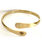 Gold cuff bracelet with paw print engraving and oval medallion logo detail