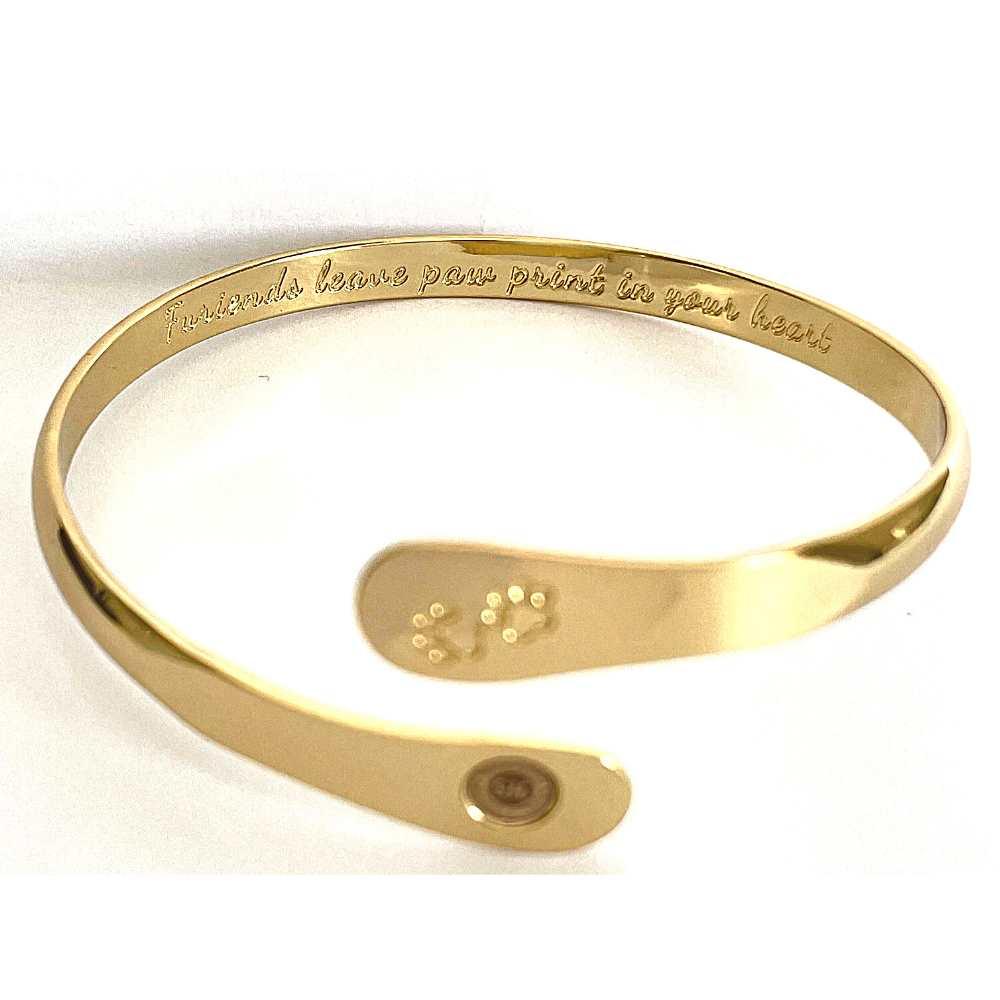 Gold cuff bracelet with paw print engraving and oval medallion logo detail