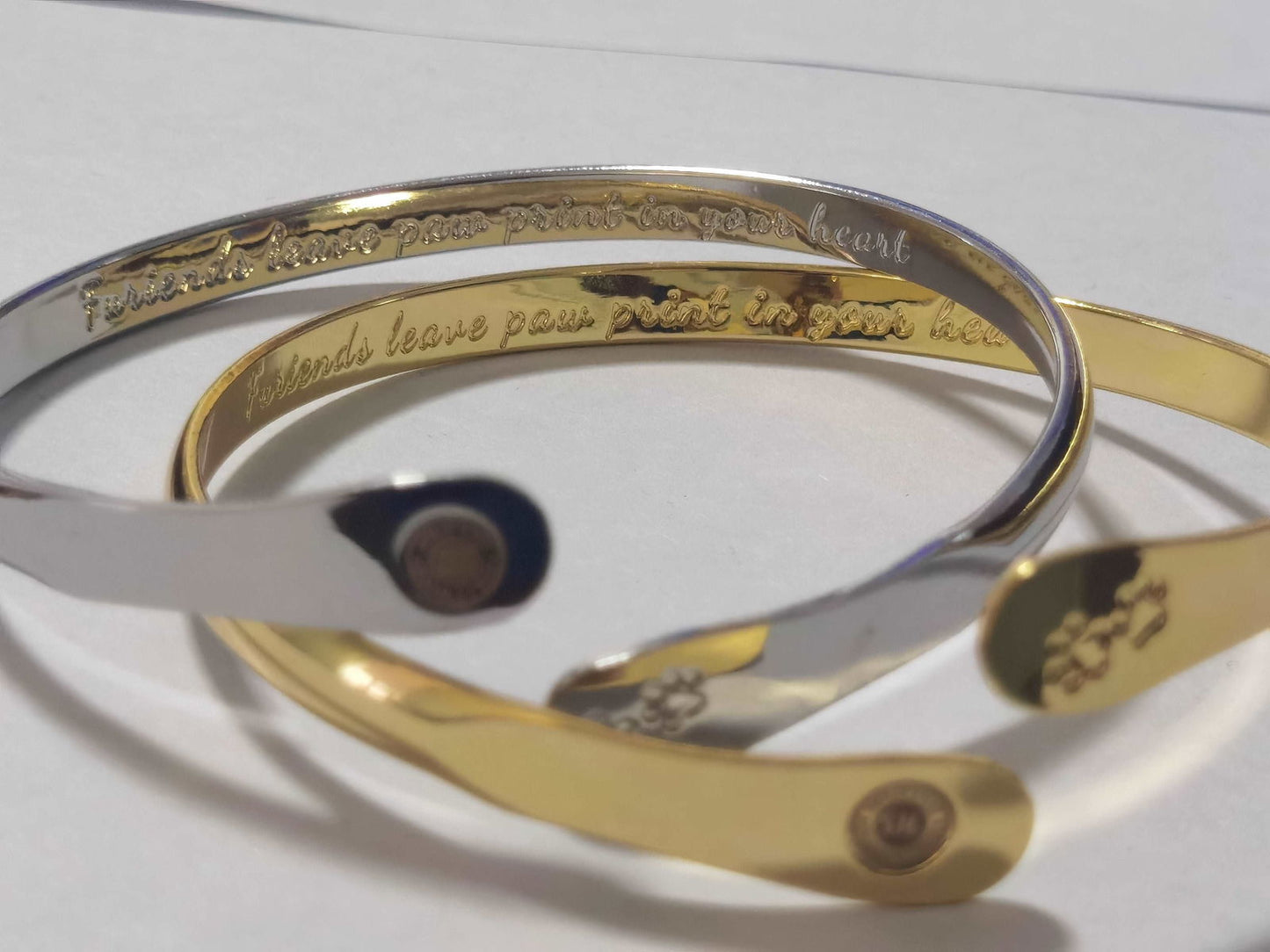 Gold cuff bracelet close-up with paw print design and oval medallion logo