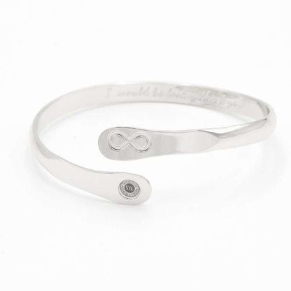 Silver infinity friendship bracelet on a flat surface, engraved infinity emblem and round logo tag.