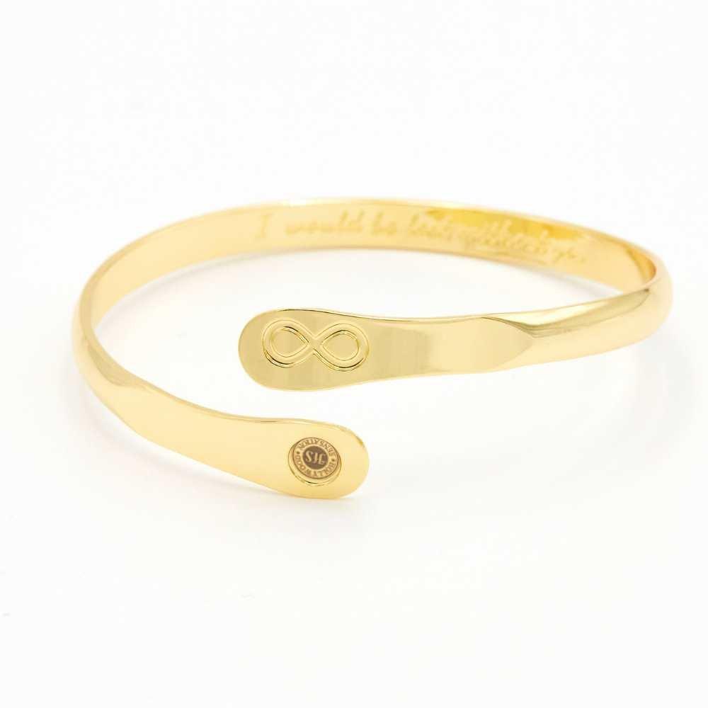 Gold infinity friendship bracelet on a flat surface, engraved infinity emblem and round logo tag.